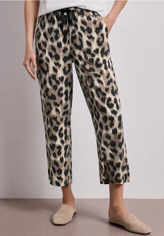 Beine in lässigen, gerade geschnittenen Leopardenmuster-Hosen mit Gürtelband, kombiniert mit beigen Slippern.
