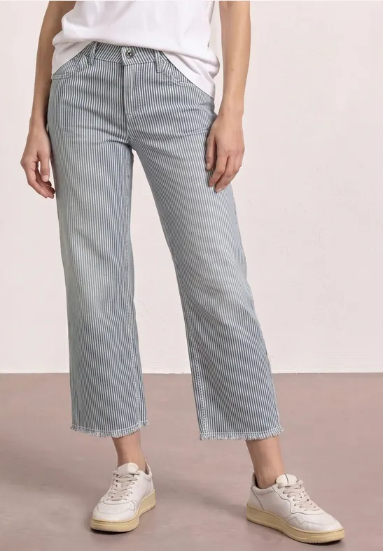 Helle, gerade geschnittene Jeans mit fransigem Saum, leicht cropped, kombiniert mit weißen Sneakern.