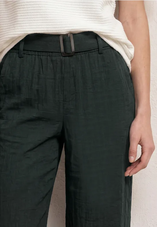 Eine Person trägt eine weiße gestreifte Bluse und schwarze Hose mit Gürtel, Bildausschnitt vom Oberkörper.