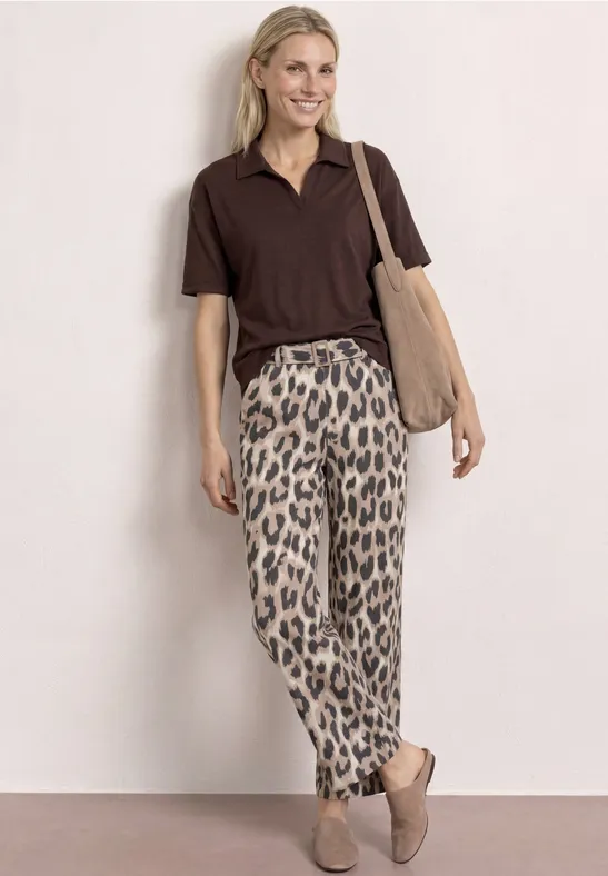 Model draagt bruin poloshirt, luipaardprint broek, beige tas en instappers