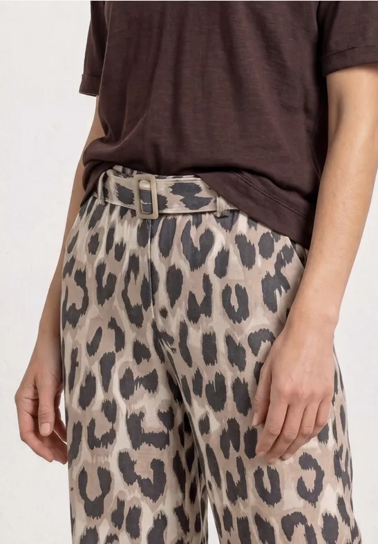 Een persoon draagt een bruin T-shirt en een luipaardprintbroek met riem.