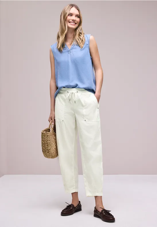 Vrouw in losse zomerkleding met rieten tas voor effen achtergrond.