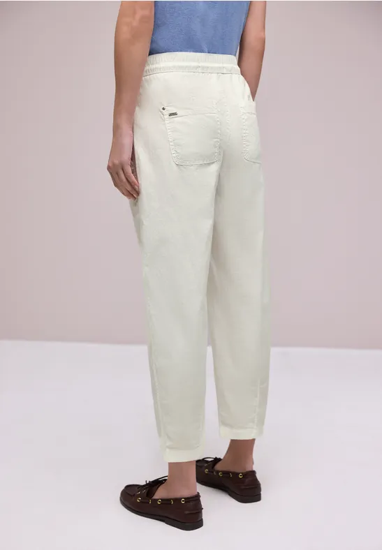 Rugaanzicht van een persoon met losse witte broek en bruine loafers.