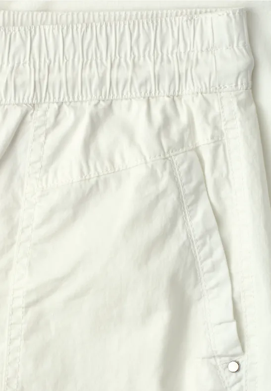 Close-up van een witte broek met elastische tailleband en schuine zijzak met drukknop.