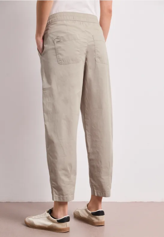 Achteraanzicht van een persoon met beige, loszittende broek met elastische taille en enkels.