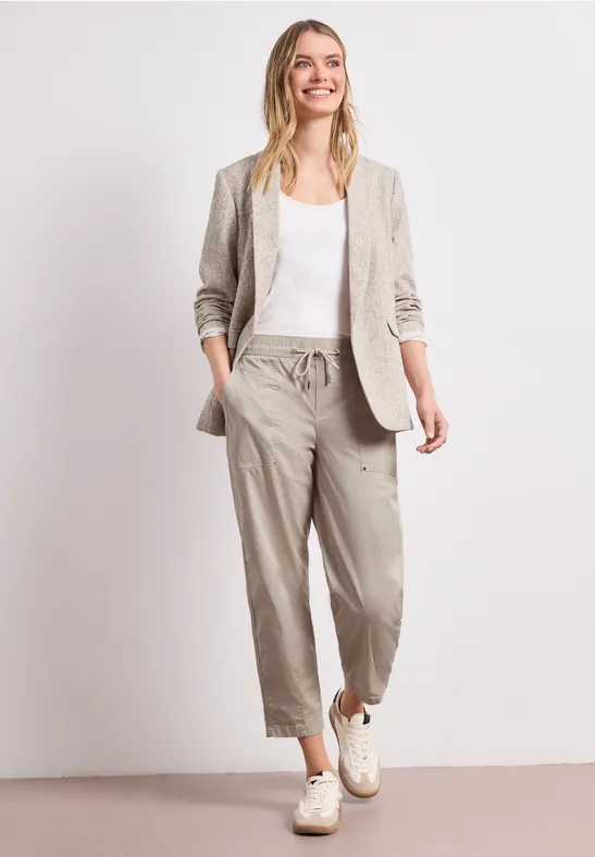Een vrouw draagt een beige linnen broek, witte top, beige blazer en witte sneakers.