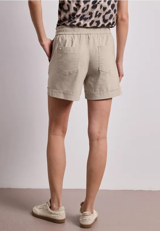 Rückansicht einer Person in beigen Leinen-Shorts und Leoparden-Top mit weißen Sneakers.