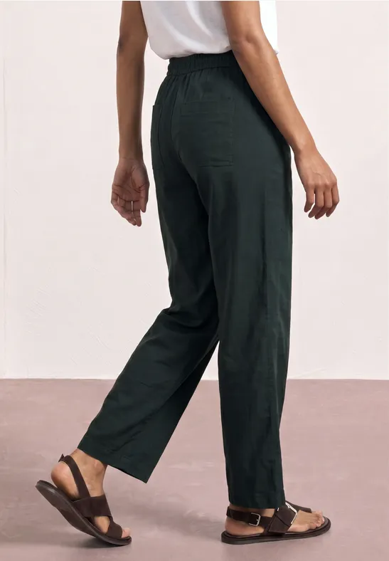 Eine Person trägt schwarze, locker sitzende Hose und braune Sandalen vor hellem Hintergrund.