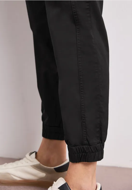 Close-up van enkels in zwarte trainingsbroek en witte sneakers.