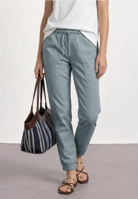 Vrouw draagt witte top, lichtblauwe broek, gestreepte tas en sandalen.