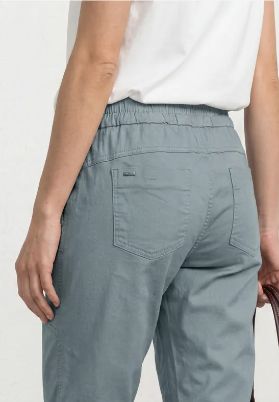Achteraanzicht: blauwgrijze chino met elastische taille en achterzakken, gecombineerd met een wit shirt.