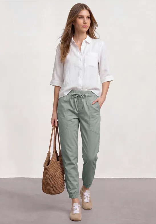Vrouw in wit overhemd en groene broek met gevlochten tas, casual en elegant