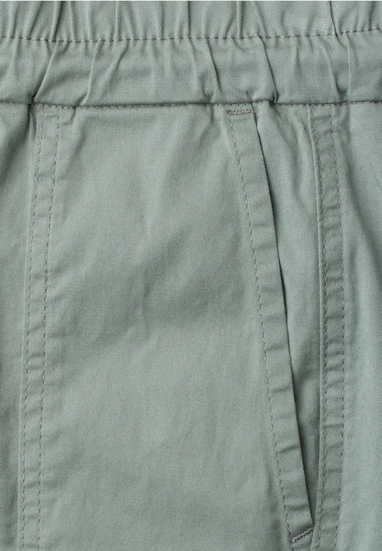 Close-up van een lichtgrijze broek met elastische taille en zijzak.