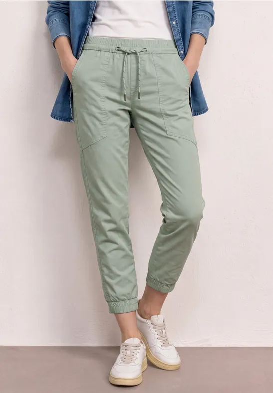 Person trägt hellgrüne Chinohose und weiße Sneakers.