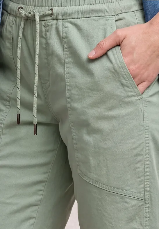 Nahaufnahme einer Person in hellgrüner Hose mit Kordelzug und Hand in der vorderen Tasche.