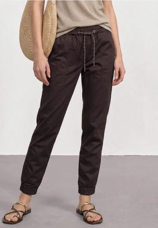 Persoon in losse, donkere joggingbroek met tunnelkoord, beige sandalen en strozak.