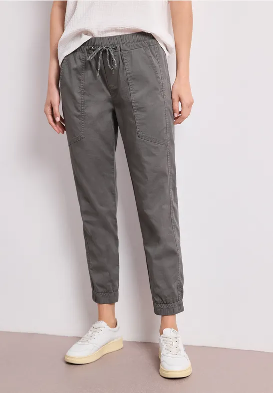 Persoon draagt een grijze, losse broek met trekkoord en witte sneakers.