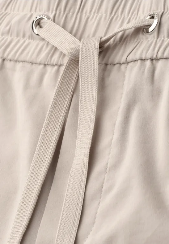 Close-up van een beige broek met tunnelkoord.