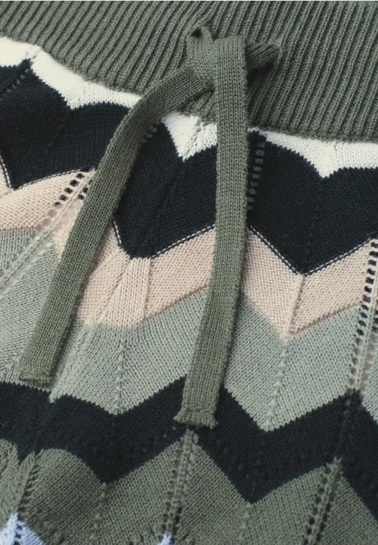 Close-up van een gebreid kledingstuk met chevronpatroon in groen, zwart en beige met trekkoordsysteem.