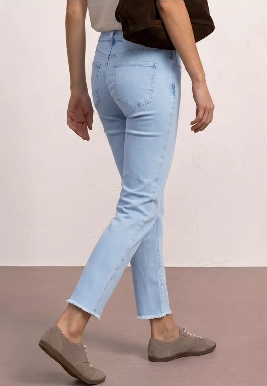 Person trägt helle Jeans, braune Slipper und eine Schultertasche vor hellem Hintergrund.