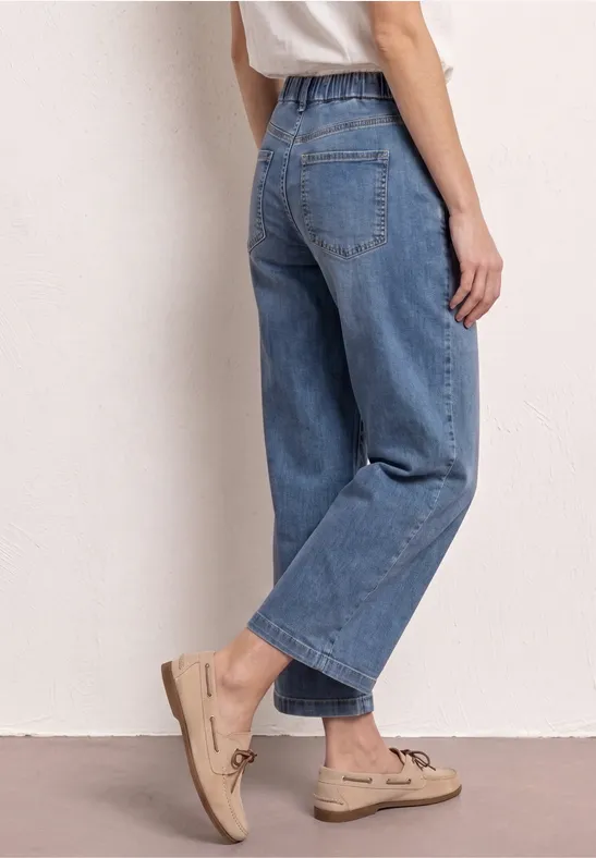 Vrouw in losse blauwe wijde jeans en beige loafers, zijaanzicht.