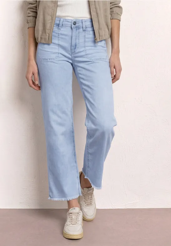 Iemand draagt lichte, wijd uitlopende jeans met rafelige zoom en witte sneakers.