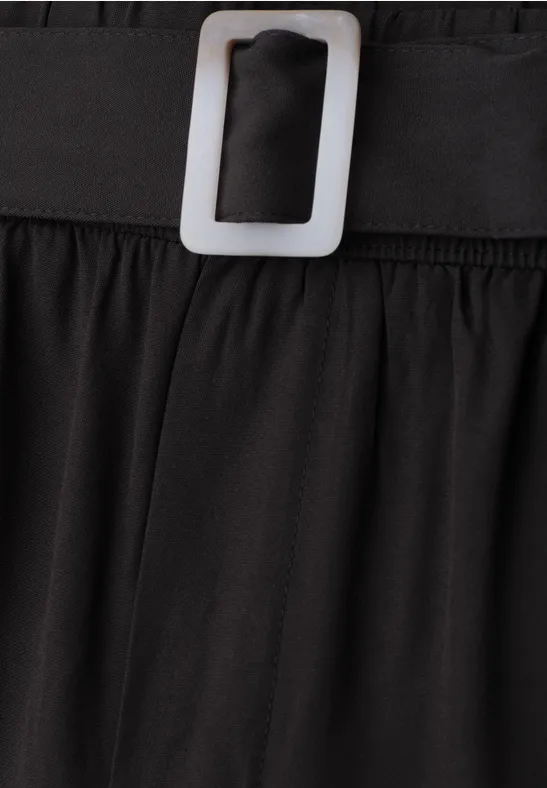 Close-up van zwart kledingstuk met elastische tailleband en zilverkleurige rechthoeksgesp.