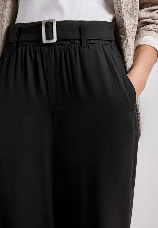 Zwarte, hooggetailleerde broek met riem en zijzakken, gecombineerd met een licht topje en vest.