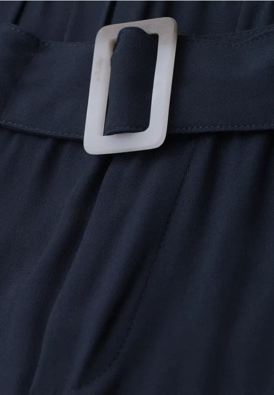 Close-up van een zwarte stoffen riem met een zilverkleurige rechthoekige gesp op een donkere stof.