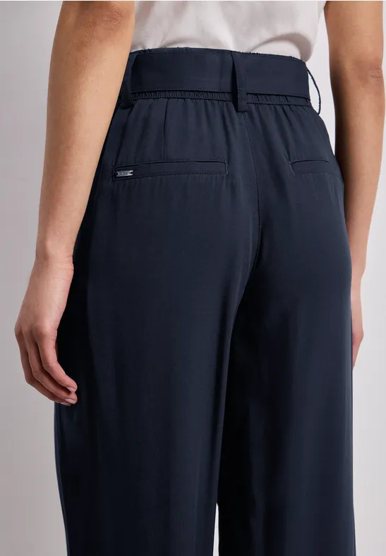 Achteraanzicht: persoon draagt een donkerblauwe, wijde broek met hoge taille en riem.