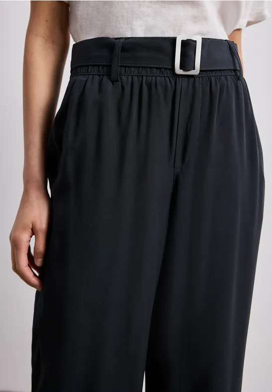 Schwarze, locker geschnittene Hose mit hohem Bund und silberner Rechteck-Gürtelschnalle.