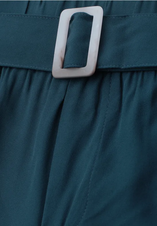 Nahaufnahme eines türkisfarbenen Gürtels aus Stoff mit weißer, rechteckiger Schnalle.