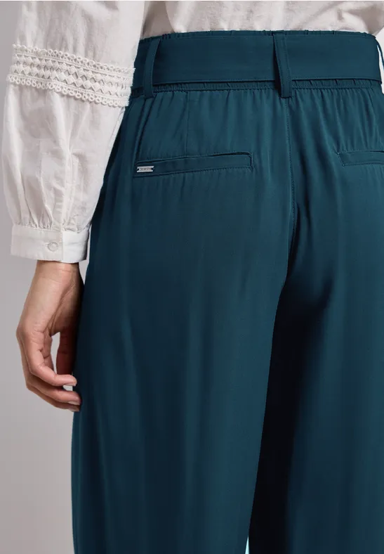 Rückansicht einer Frau in weißer Bluse mit Stickereien und tiefpetrolfarbenen Hosen mit Gummibund.