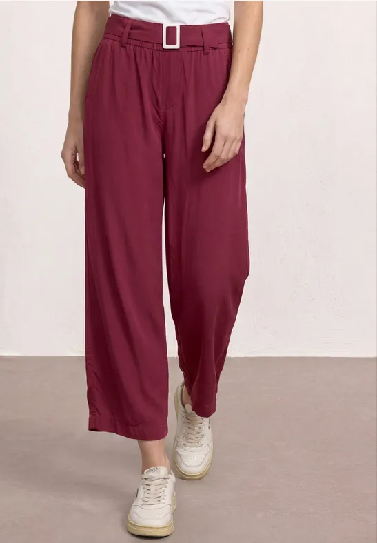 Weinrote, hoch taillierte, weite Hose mit Gürtel und Bundfalten, kombiniert mit weißen Sneakern.