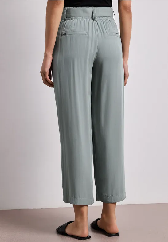 Graue, weite Hose mit elastischem Bund und Bügelfalten, kombiniert mit schwarzen Pantoletten.