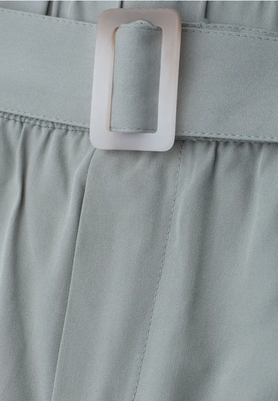 Nahaufnahme eines hellgrauen Bundes mit feinen Falten und einem passenden Gürtel mit rechteckiger Schnalle.