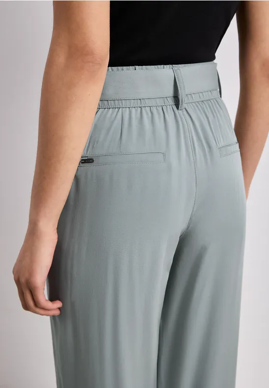 Rückansicht einer Person in hellgrauen, lockeren, hoch geschnittenen Hose mit Gummizug und Gesäßtaschen.