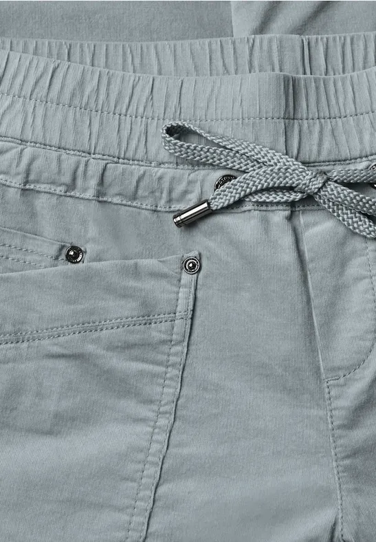 Nahaufnahme einer grauen Jogginghose mit Kordelzug, Bundfalten und Taschen mit Nieten