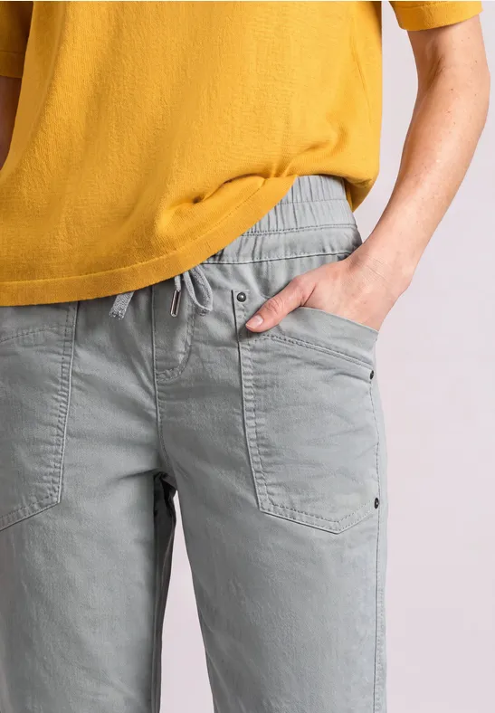 Person trägt graue Freizeithose mit Taschen und senfgelbes T-Shirt, Ausschnitt von Brust bis Hüfte.