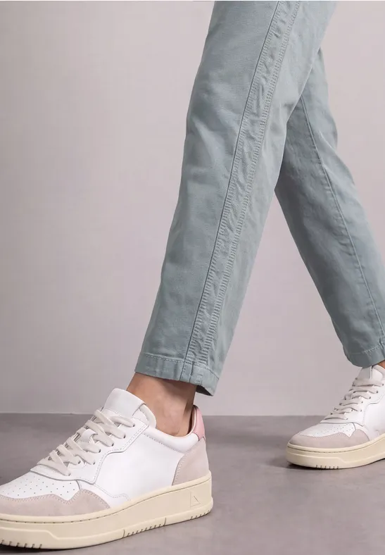Weiße Sneaker mit beigen Sohlen, getragen zu hellgrünen, knöchellangen Hosen.