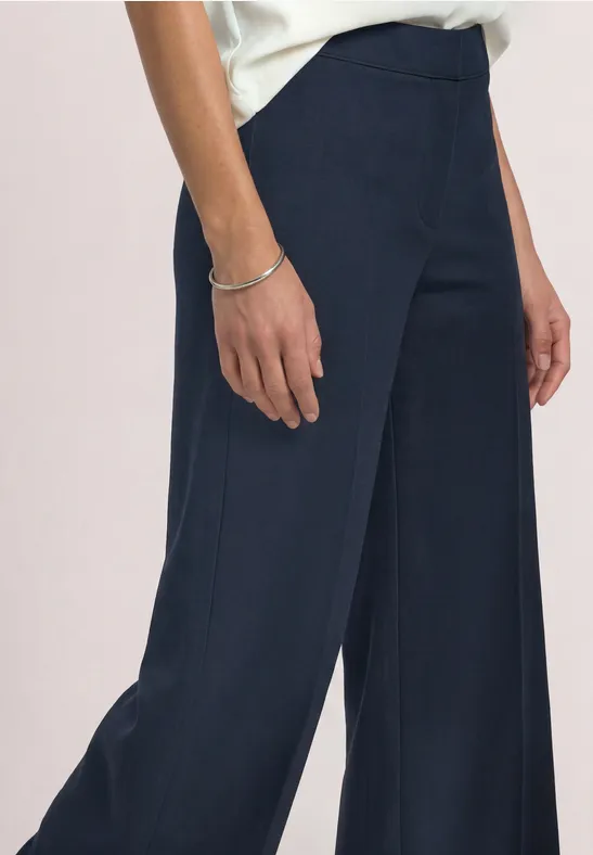 Damenkörper ab Taille in dunkelblauer, weiter Hose mit silbernem Armband am Handgelenk.