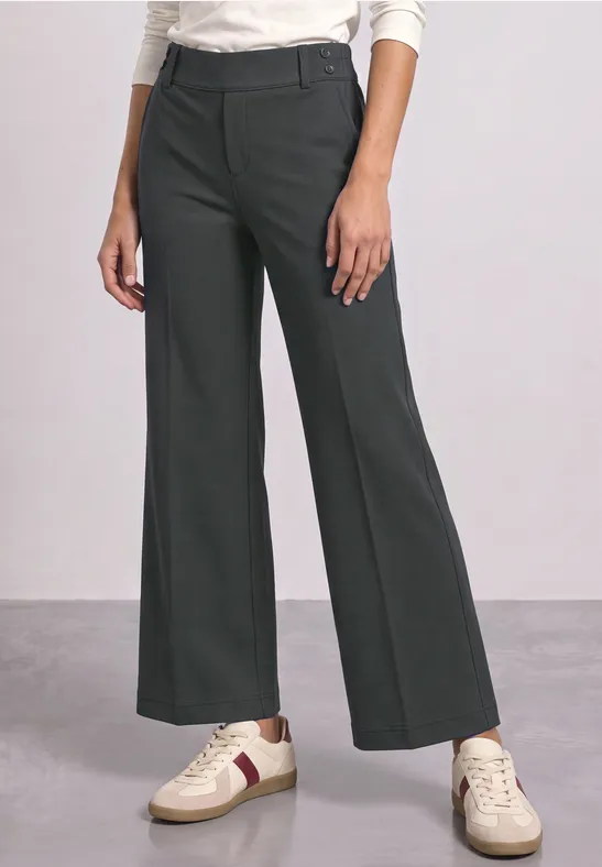 Dunkelgraue, weite High-Waist-Hose kombiniert mit weißem Langarmshirt und sportlichen Sneakern.