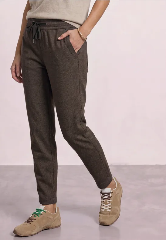 Dunkelbraune Leinenhose mit Tunnelzug, schmale Passform und Seitentaschen, kombiniert mit beigen Sneakers.