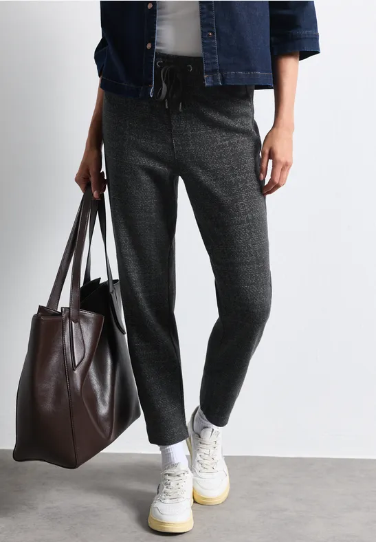 Person trägt graue, locker geschnittene Hose, weiße Sportschuhe und hält eine große braune Tasche.