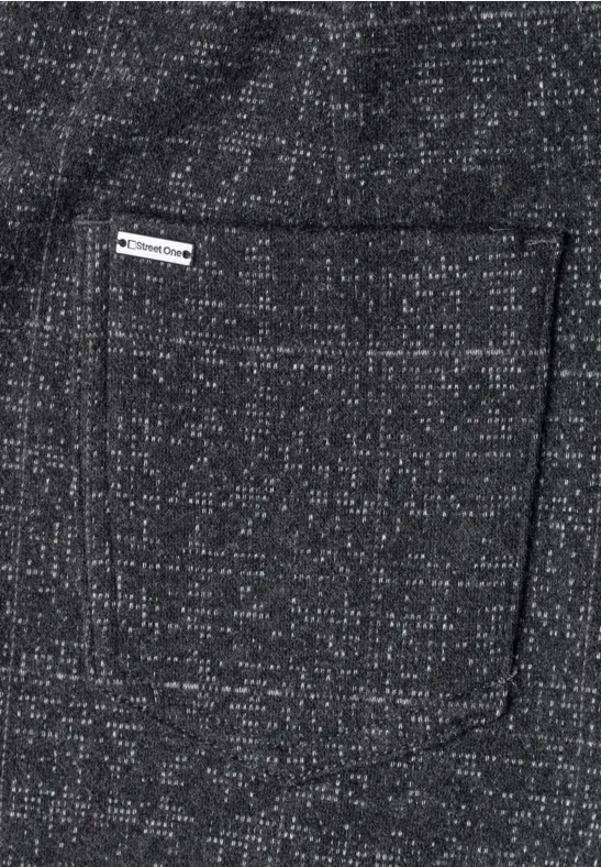 Auf grauem, meliertem Stoff mit weißen Sprenkeln ist eine eckige Tasche mit kleinem Webetikett angebracht.