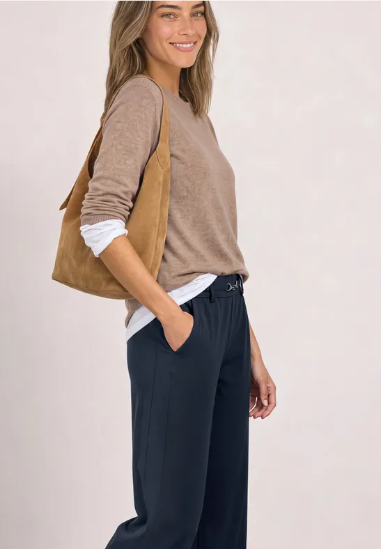 Eine Frau trägt navyblaue Jogginghosen, ein hellbraunes Langarmshirt und eine passende Wildledertasche.