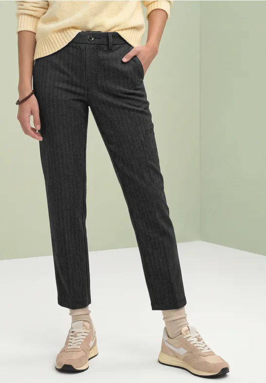 Pantalon noir à fines rayures porté avec un pull jaune pâle et des baskets beiges.