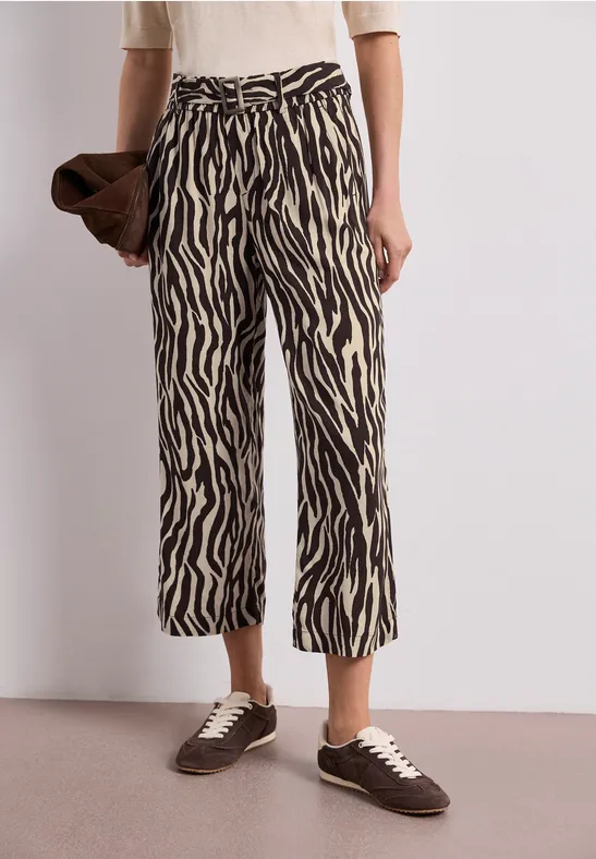 Croppte Hose mit Zebra-Print, weißes Oberteil, braune Clutch und braune Sneaker.