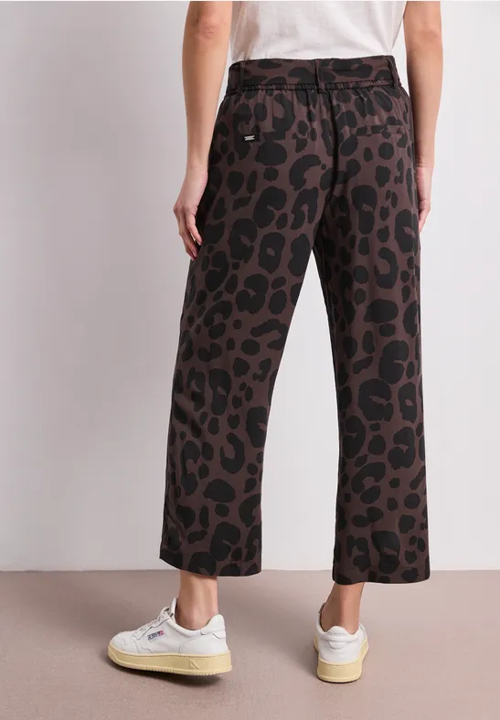 Rückenansicht: Person trägt weiße Sneaker, Culotte-Hose mit braun-schwarzem Leopardenmuster und weißes T-Shirt.