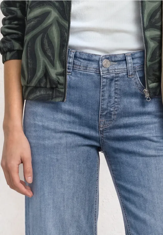 Person trägt hochgeschnittene blaue Jeans, weißes Shirt und grüne Camouflage-Jacke.